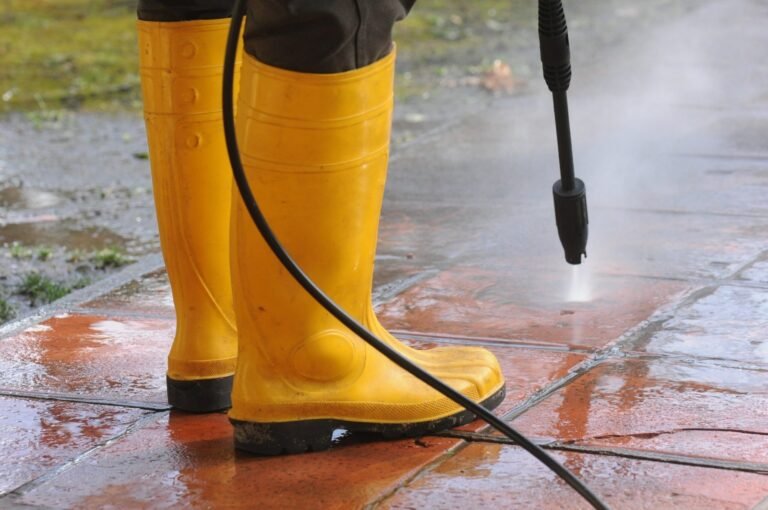person-wearing-yellow-rubber-boots-with-high-pressure-water-nozzle-cleaning-dirt-tiles-scaled
